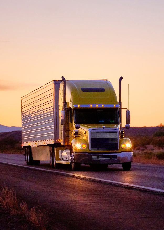 A Semi truck on the road featuring an orange sunset in the desert
